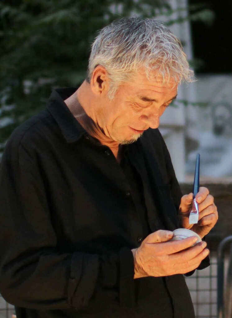 Künstler Jörg Düsterwald hält einen Pinsel und einen Farbtopf in der Hand.