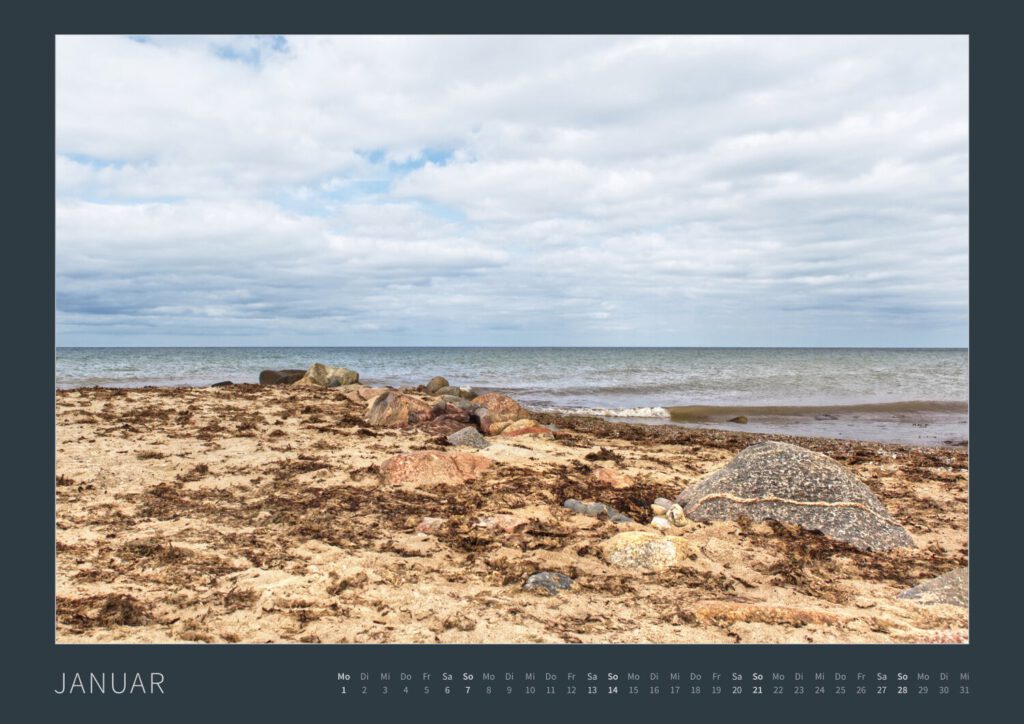 Das Monatsblatt Januar vom Bodypainting-Kalender NATURE ART 2024 von Künstler Jörg Düsterwald. Ein bemaltes Fotomodell liegt am Strand zwischen Steinen.