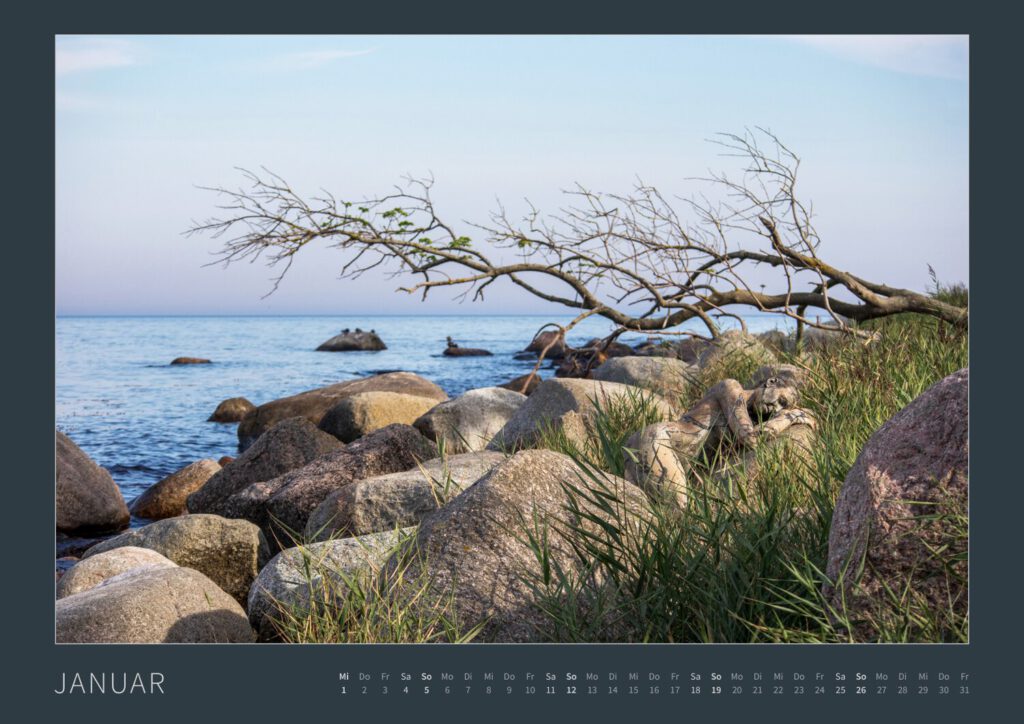 Das Monatsblatt Januar 2025 vom Bodypainting-Kalender NATURE ART 2024 von Künstler Jörg Düsterwald. Ein bemaltes Fotomodell liegt zwischen großen Steinen an einer Küste.