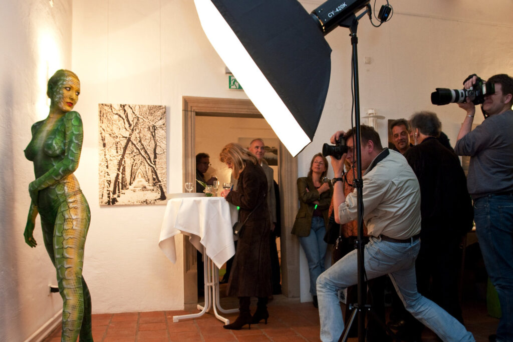 Während einer Kunstausstellung hat der Künstler Jörg Düsterwald ein nacktes Fotomodell vollständig mit Farbe bemalt. Die Frau posiert vor einer Wand und wird von einem Scheinwerfer beleuchtet. Fotografen richten ihre Kameras auf sie, während Gäste der Veranstaltung der Aktion zuschauen.