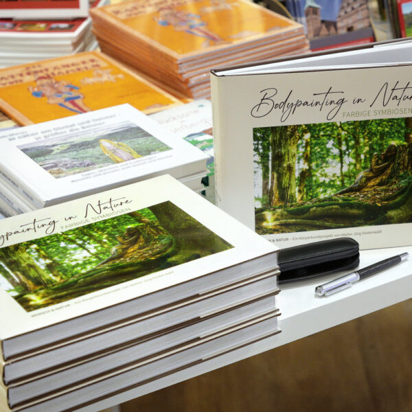 Künstler Jörg Düsterwald hat von dem Körperkunstprojekt Nature Art einen Fotobildband publiziert. Einige Bücher sind auf einem Tisch gestapelt und aufgestellt.