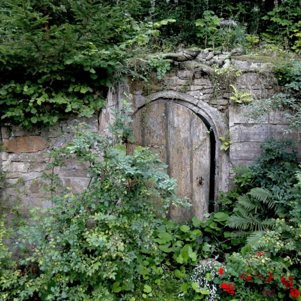 Für das Kunstprojekt DOOR ART ließ sich ein nacktes Fotomodell von Künstler Jörg Düsterwald vollständig so mit Farbe bemalen, dass es genau zur Umgebung von Türen und Toren passt. Die Frau liegt auf einer Steinmauer über einer verwitterten Holztür.