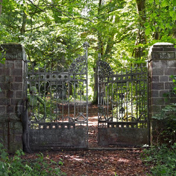 Für das Kunstprojekt DOOR ART ließ sich ein nacktes Fotomodell von Künstler Jörg Düsterwald vollständig so mit Farbe bemalen, dass es genau zur Umgebung von Türen und Toren passt. Die Frau steht an einem Steinpfosten vor einem großen Eisentor eines Parks.