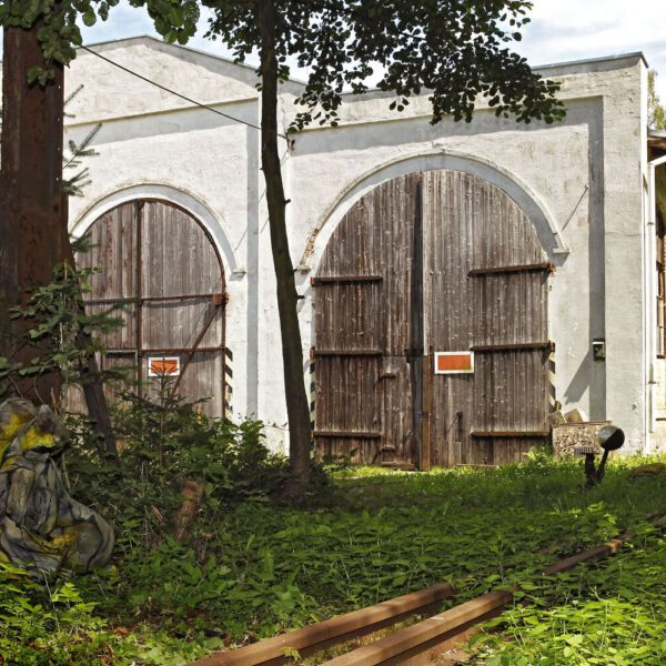 Für das Kunstprojekt DOOR ART ließen sich zwei nackte Fotomodelle von Künstler Jörg Düsterwald vollständig so mit Farbe bemalen, dass sie genau zur Umgebung von Türen und Toren passen. Sie sitzen eng umschlungen im Gebüsch vor einem Lokschuppen.