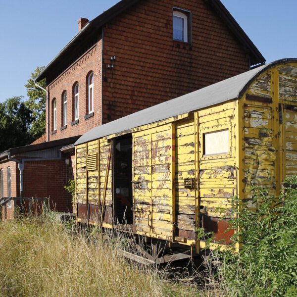 Für das Kunstprojekt DOOR ART ließ sich ein nacktes Fotomodell von Künstler Jörg Düsterwald vollständig so mit Farbe bemalen, dass es genau zur Umgebung von Türen und Toren passt. Die Frau steht an einem alten, gelben Güterwaggon auf einem verlassenen Bahnhof.
