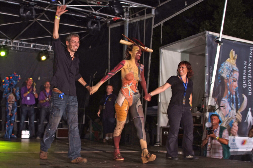 Künstler Jörg Düsterwald gewinnt mit seinem Team die Deutsche Bodypainting-Meisterschaft. Zusammen jubeln sie auf der Bühne.