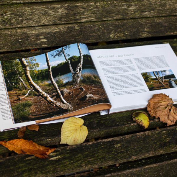 Künstler Jörg Düsterwald hat von dem Körperkunstprojekt Nature Art einen Fotobildband publiziert. Das Buch liegt aufgeschlagen auf einer Bank mit Herbstlaub.