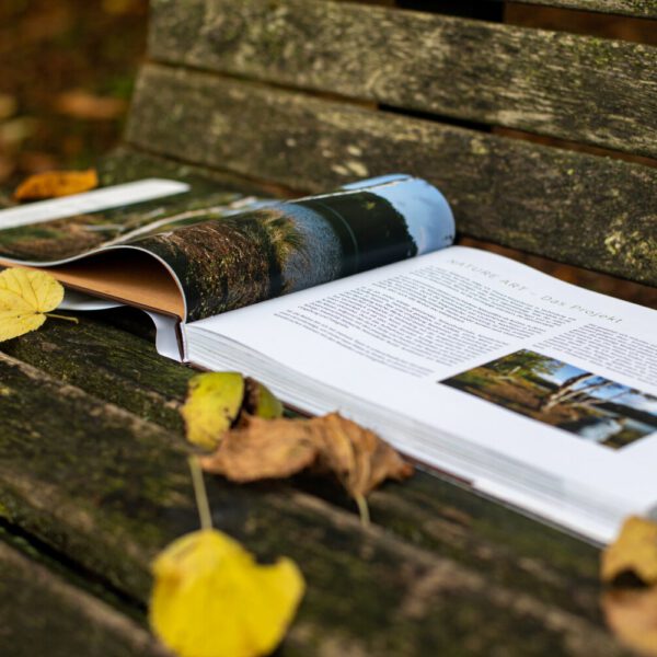 Künstler Jörg Düsterwald hat von dem Körperkunstprojekt Nature Art einen Fotobildband publiziert. Das Buch liegt aufgeschlagen auf einer Bank mit Herbstlaub.