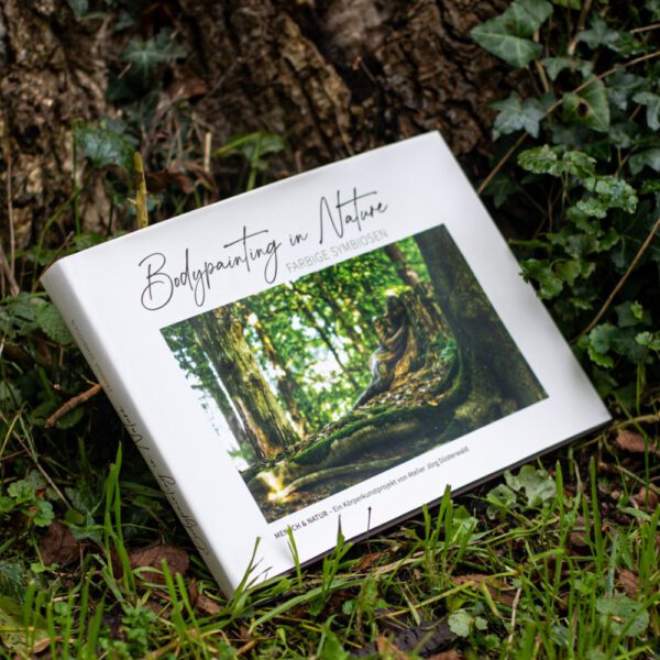 Künstler Jörg Düsterwald hat von dem Körperkunstprojekt Nature Art einen Fotobildband publiziert. Das Buch liegt im Gras an einem Baumstamm.