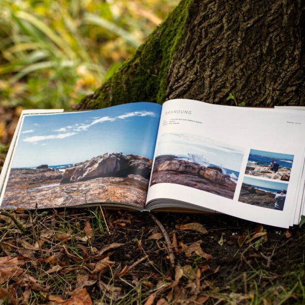 Künstler Jörg Düsterwald hat von dem Körperkunstprojekt Nature Art einen Fotobildband publiziert. Das Buch liegt aufgeschlagen im Laub an einem Baumstamm.
