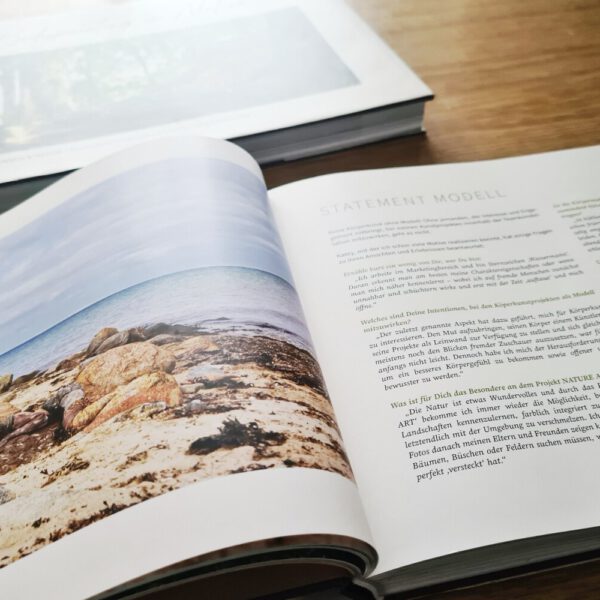 Künstler Jörg Düsterwald hat von dem Körperkunstprojekt Nature Art einen Fotobildband publiziert. Das Buch liegt auf einem Tisch, einige Seiten sind beispielhaft aufgeschlagen.