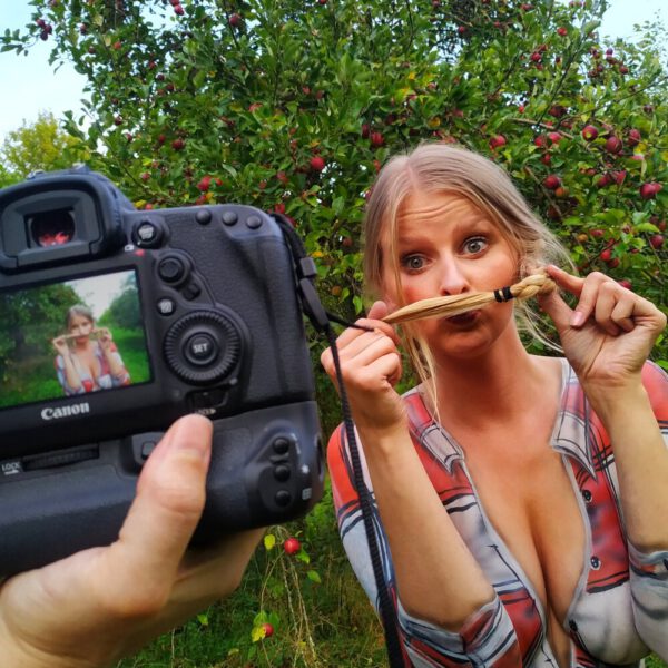 Im Rahmen des Kunstprojektes AGRAR ART hat Bodypaint-Künstler Jörg Düsterwald ein nacktes Fotomodell mit Körperfarbe so bemalt, als hätte die Frau eine kurze blaue Hose und ein rotweiß-kariertes Hemd an. Sie befindet sich in einer Apfelbaumplantage und erntet die Äpfel.