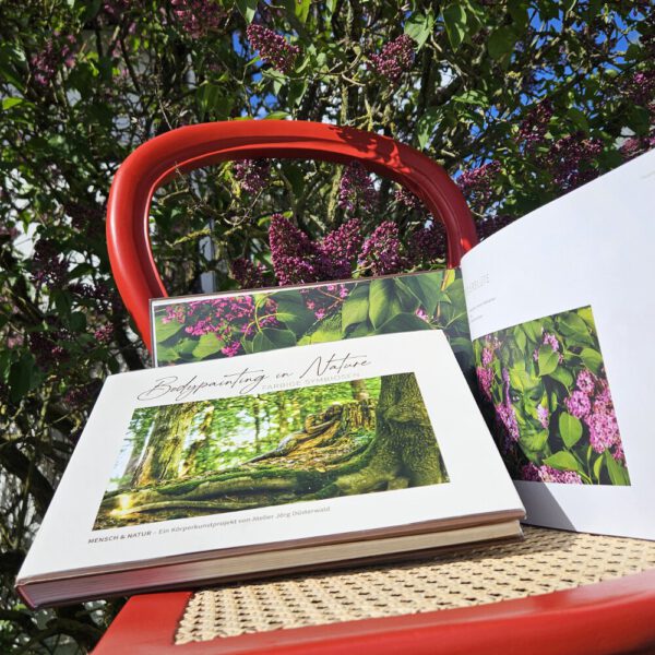 Das Buch BODYPAINTING IN NATURE von Künstler Jörg Düsterwald wird mit einem roten Stuhl an einem Originalplatz des Kunstprojektes NATURE ART gezeigt.