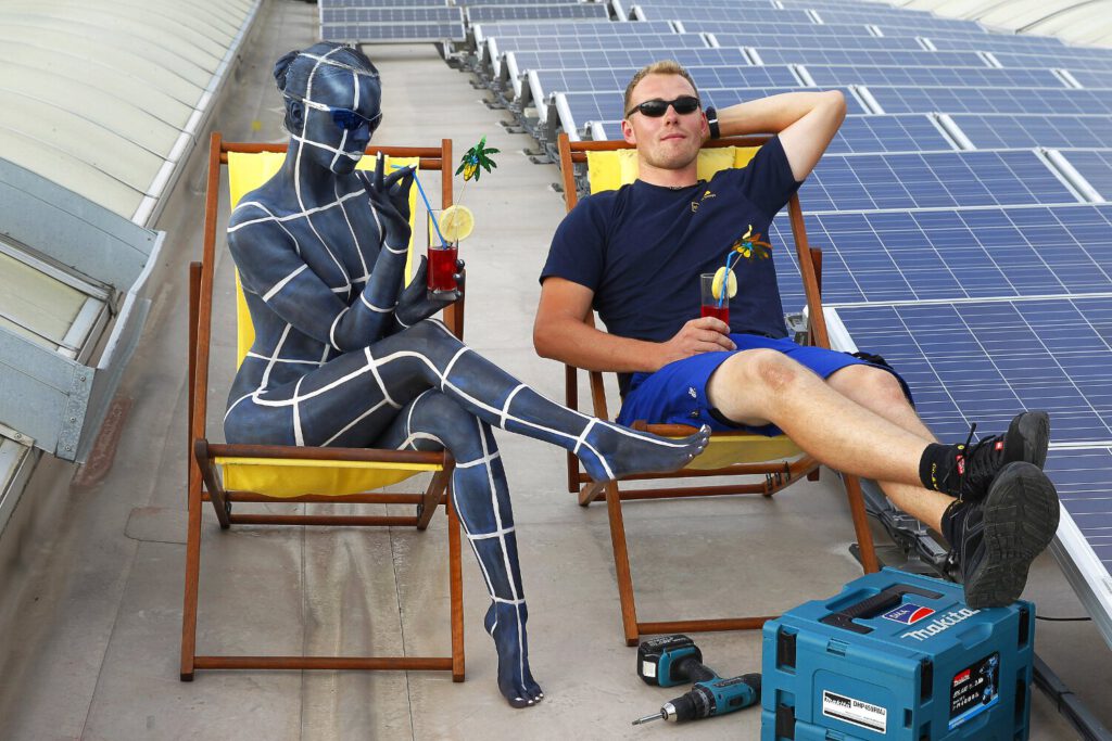 Für das Kunstprojekt WORKING ART, bei dem Berufe mit Bodypaintingmodellen dargestellt werden, hat Künstler Jörg Düsterwald ein Fotomodell vollständig bemalt. Die gestylte Frau trägt ein Solarpanel-Muster und hält sich zusammen mit einem Monteur bei einer Photovoltaikanlage auf.