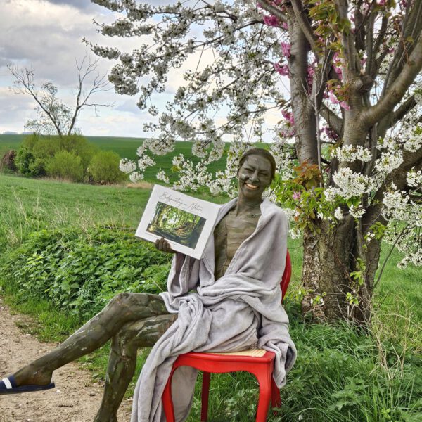 Das Buch BODYPAINTING IN NATURE von Künstler Jörg Düsterwald wird mit einem roten Stuhl an einem Originalplatz des Kunstprojektes NATURE ART gezeigt.