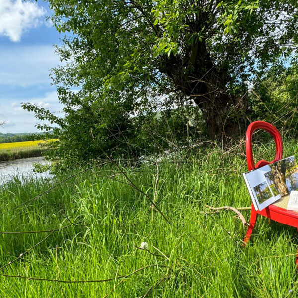 Das Buch BODYPAINTING IN NATURE von Künstler Jörg Düsterwald wird mit einem roten Stuhl an einem Originalplatz des Kunstprojektes NATURE ART gezeigt.