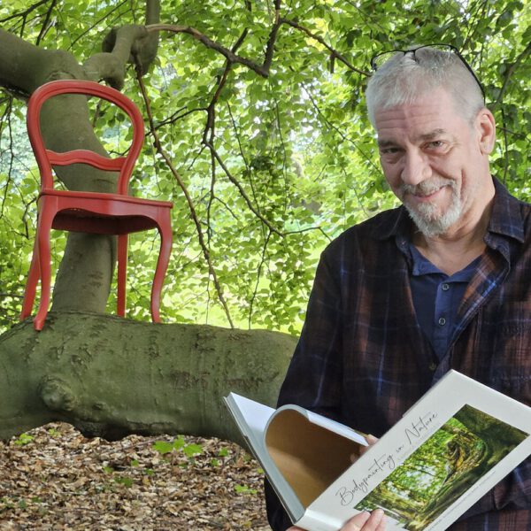 Das Buch BODYPAINTING IN NATURE von Künstler Jörg Düsterwald wird mit einem roten Stuhl an einem Originalplatz des Kunstprojektes NATURE ART gezeigt.