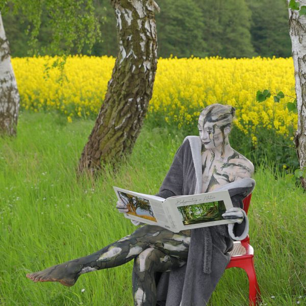 Das Buch BODYPAINTING IN NATURE von Künstler Jörg Düsterwald wird mit einem roten Stuhl an einem Originalplatz des Kunstprojektes NATURE ART gezeigt.