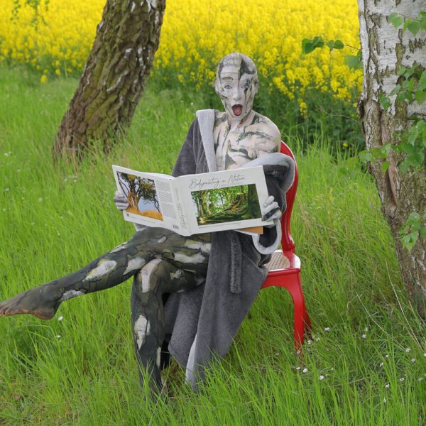 Das Buch BODYPAINTING IN NATURE von Künstler Jörg Düsterwald wird mit einem roten Stuhl an einem Originalplatz des Kunstprojektes NATURE ART gezeigt.