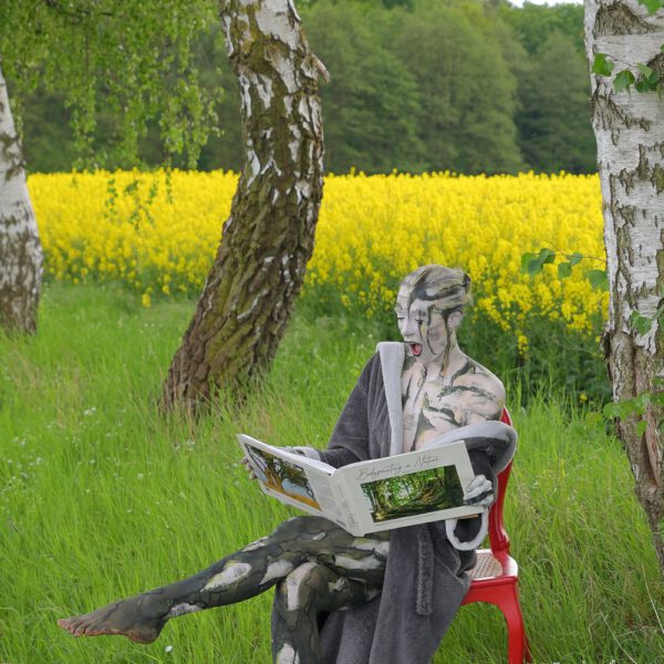 Das Buch BODYPAINTING IN NATURE von Künstler Jörg Düsterwald wird mit einem roten Stuhl an einem Originalplatz des Kunstprojektes NATURE ART gezeigt.