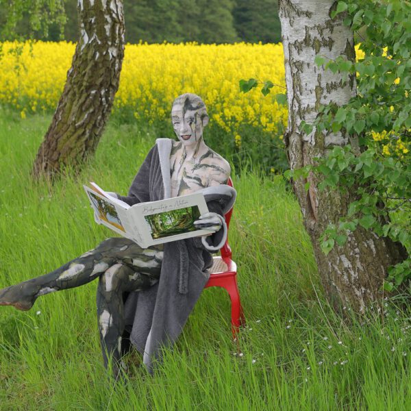 Das Buch BODYPAINTING IN NATURE von Künstler Jörg Düsterwald wird mit einem roten Stuhl an einem Originalplatz des Kunstprojektes NATURE ART gezeigt.