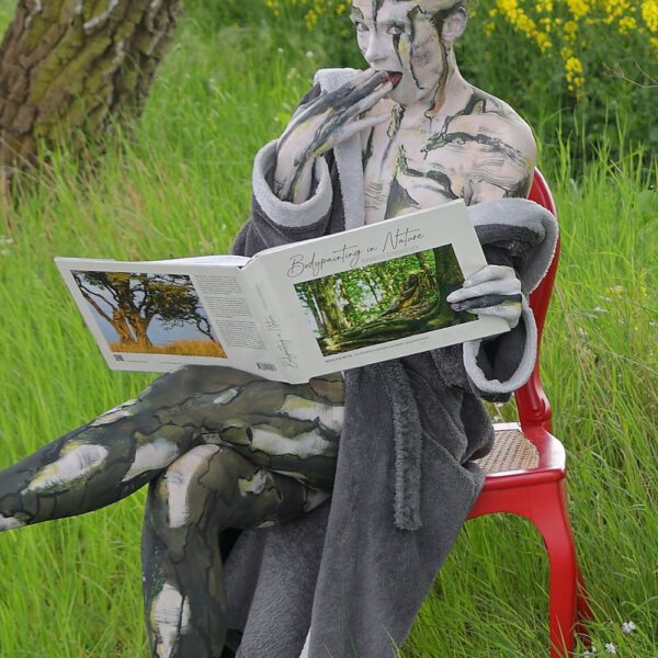 Das Buch BODYPAINTING IN NATURE von Künstler Jörg Düsterwald wird mit einem roten Stuhl an einem Originalplatz des Kunstprojektes NATURE ART gezeigt.