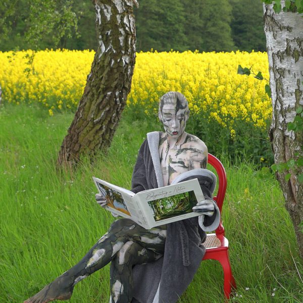 Das Buch BODYPAINTING IN NATURE von Künstler Jörg Düsterwald wird mit einem roten Stuhl an einem Originalplatz des Kunstprojektes NATURE ART gezeigt.