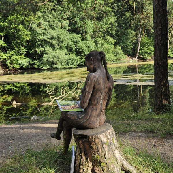 Ein Fotomodell ist mit Farbe der Kulisse angepasst und liest im Buch BODYPAINTING IN NATURE von Künstler Jörg Düsterwald.