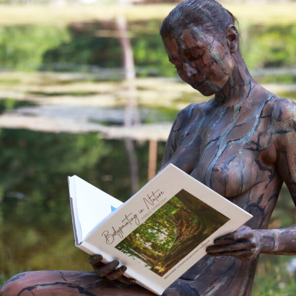 Ein Fotomodell ist mit Farbe der Kulisse angepasst und liest im Buch BODYPAINTING IN NATURE von Künstler Jörg Düsterwald.