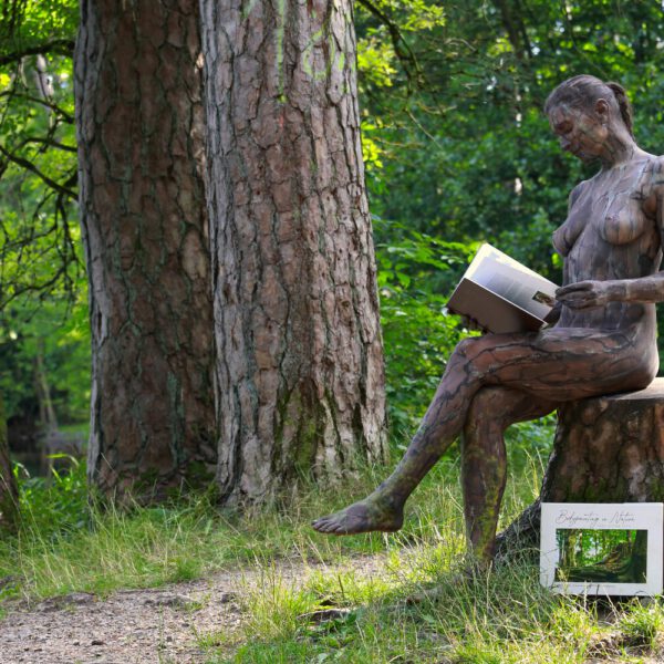 Ein Fotomodell ist mit Farbe der Kulisse angepasst und liest im Buch BODYPAINTING IN NATURE von Künstler Jörg Düsterwald.