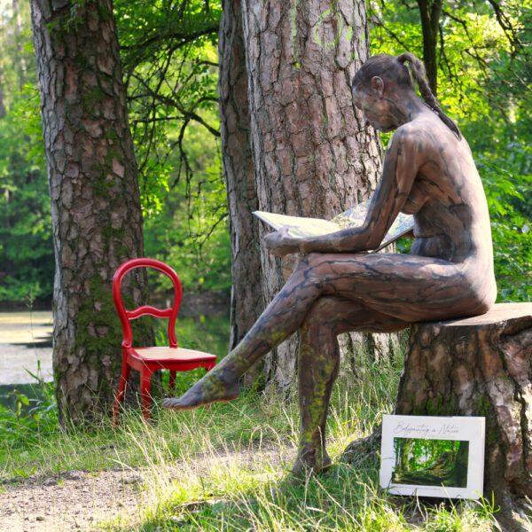 Das Buch BODYPAINTING IN NATURE von Künstler Jörg Düsterwald wird mit einem roten Stuhl an einem Originalplatz des Kunstprojektes NATURE ART gezeigt.