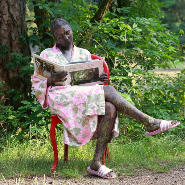 Das Buch BODYPAINTING IN NATURE von Künstler Jörg Düsterwald wird mit einem roten Stuhl an einem Originalplatz des Kunstprojektes NATURE ART gezeigt.