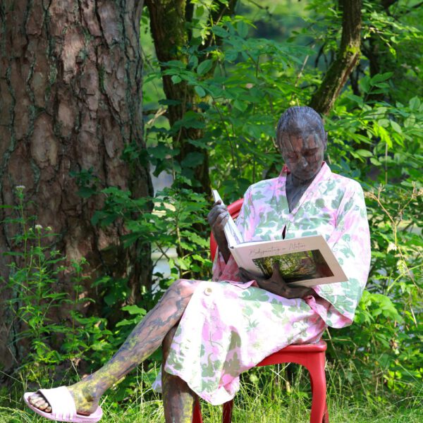 Das Buch BODYPAINTING IN NATURE von Künstler Jörg Düsterwald wird mit einem roten Stuhl an einem Originalplatz des Kunstprojektes NATURE ART gezeigt.