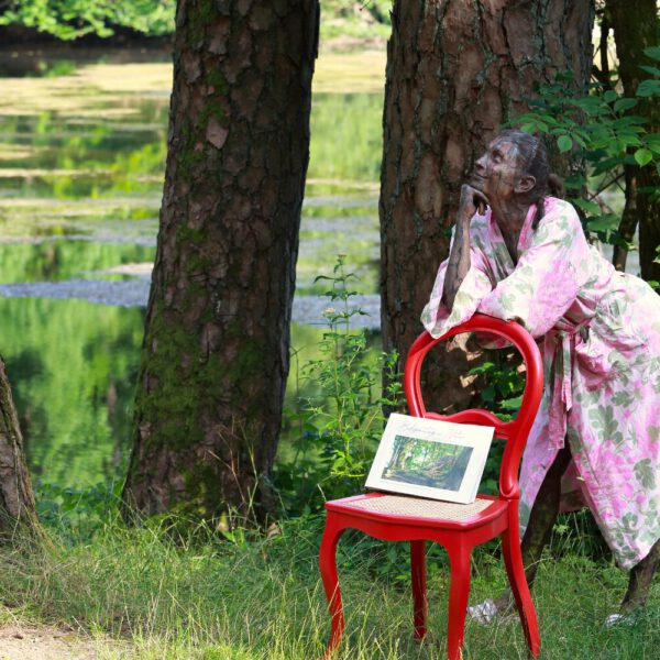 Das Buch BODYPAINTING IN NATURE von Künstler Jörg Düsterwald wird mit einem roten Stuhl an einem Originalplatz des Kunstprojektes NATURE ART gezeigt.