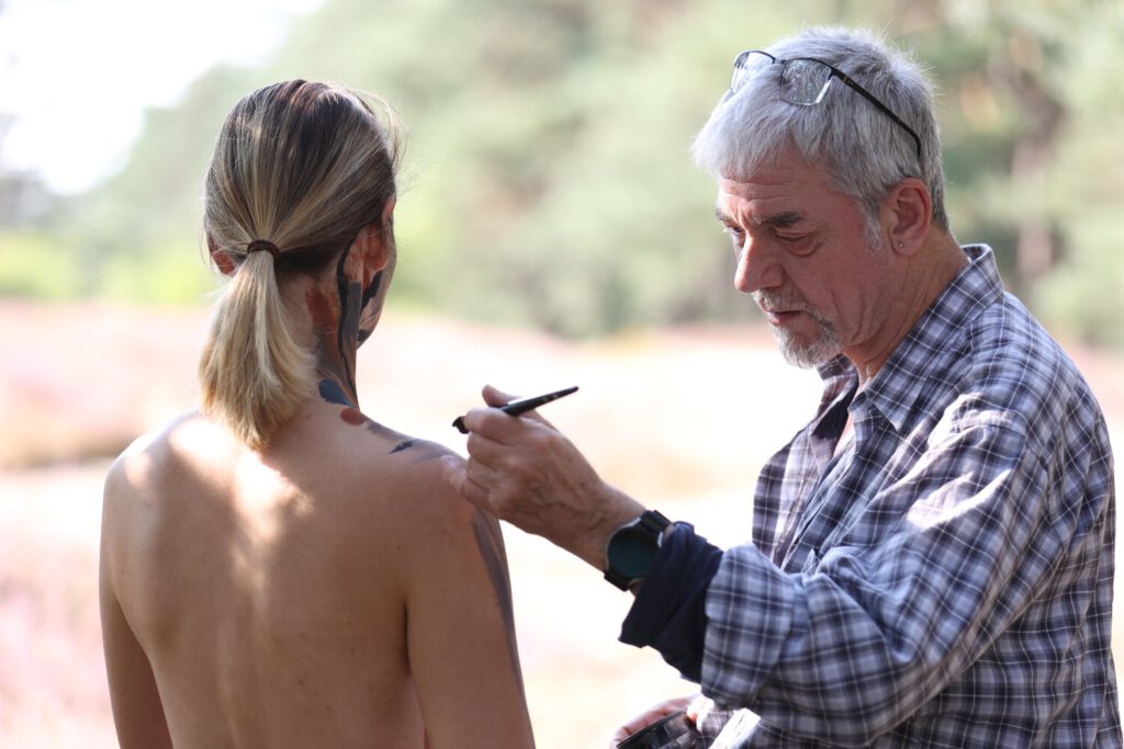 Ein nacktes Fotomodell wird für das Kunstprojekt Natureart von Künstler Jörg Düsterwald vollständig so mit Farbe bemalt, dass die Person mit der Kulisse verschmilzt.