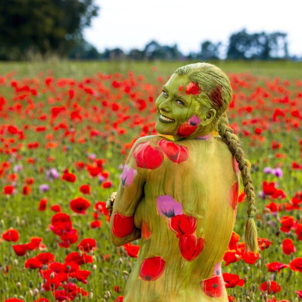 Ein bemaltes Fotomodell in einem roten Mohnfeld ergibt FARBIGE SYMBIOSEN. Ein Motiv von dem Körperkunstprojekt NATURE ART des Künstlers Jörg Düsterwald mit einem Bodypaintingmodell.