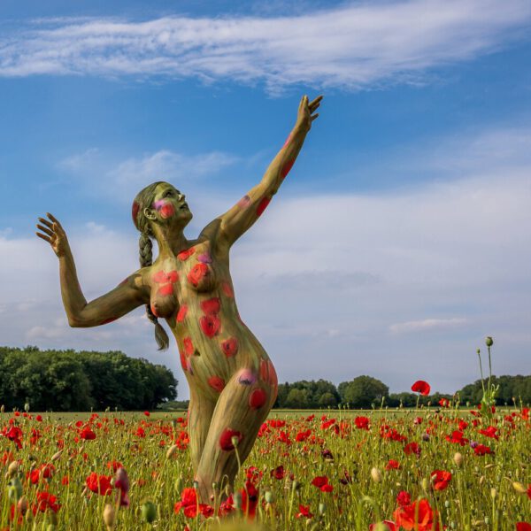 Ein bemaltes Fotomodell in einem roten Mohnfeld ergibt FARBIGE SYMBIOSEN. Ein Motiv von dem Körperkunstprojekt NATURE ART des Künstlers Jörg Düsterwald mit einem Bodypaintingmodell.