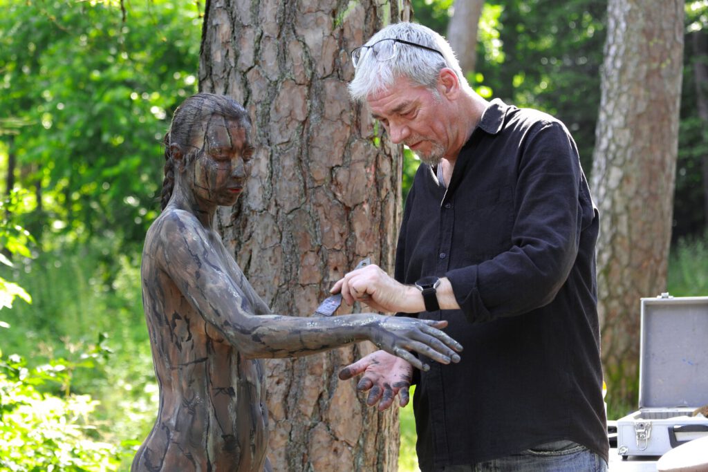 Ein nacktes Fotomodell wird für das Kunstprojekt Natureart von Künstler Jörg Düsterwald vollständig so mit Farbe bemalt, dass die Person mit der Kulisse verschmilzt.