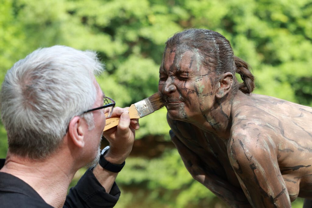 Ein nacktes Fotomodell wird für das Kunstprojekt Natureart von Künstler Jörg Düsterwald vollständig so mit Farbe bemalt, dass die Person mit der Kulisse verschmilzt.