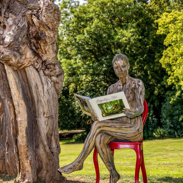 Das Buch BODYPAINTING IN NATURE von Künstler Jörg Düsterwald wird mit einem roten Stuhl an einem Originalplatz des Kunstprojektes NATURE ART gezeigt.