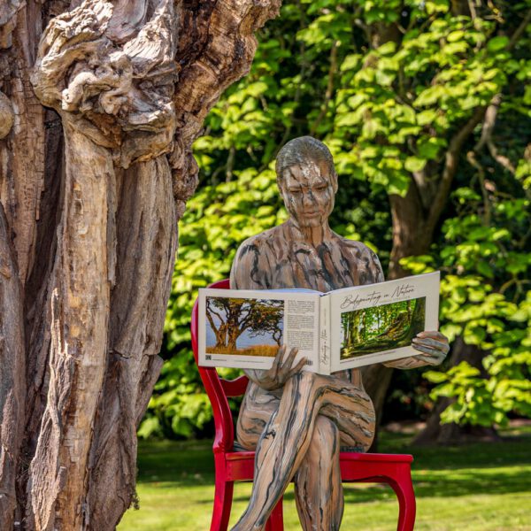 Das Buch BODYPAINTING IN NATURE von Künstler Jörg Düsterwald wird mit einem roten Stuhl an einem Originalplatz des Kunstprojektes NATURE ART gezeigt.