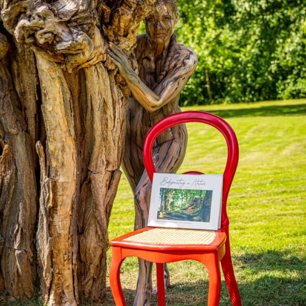Das Buch BODYPAINTING IN NATURE von Künstler Jörg Düsterwald wird mit einem roten Stuhl an einem Originalplatz des Kunstprojektes NATURE ART gezeigt.