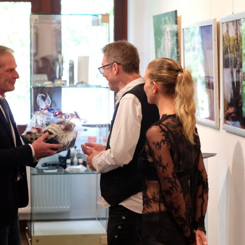 Künstler Jörg Düsterwald und seine Begleitung bekommen während der Vernissage einer Ausstellung ein Präsent überreicht.
