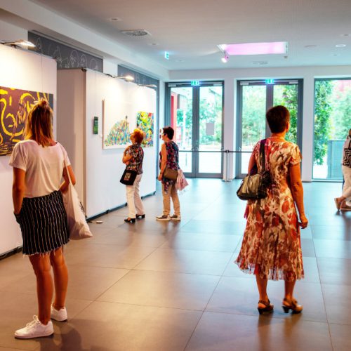 Besucherinnen und Besucher betrachten Bilder von Künstler Jörg Düsterwald, die in einer Ausstellung präsentiert werden.