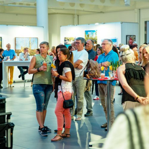 Besucherinnen und Besucher betrachten Bilder von Künstler Jörg Düsterwald, die in einer Ausstellung präsentiert werden.